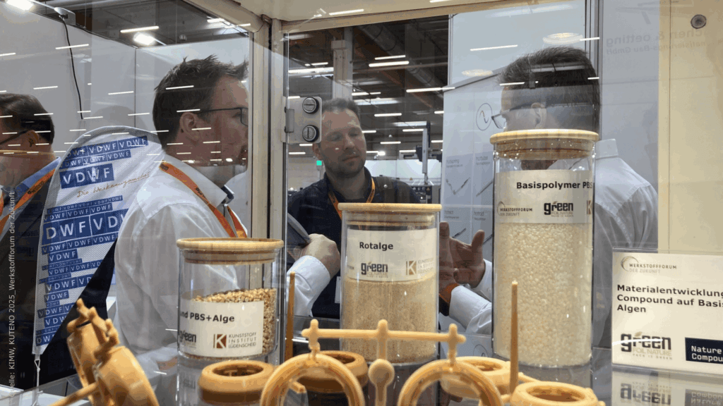 Vitrine auf der KUTENO 2025 mit Exponaten, dahinter sich unterhaltende Personen